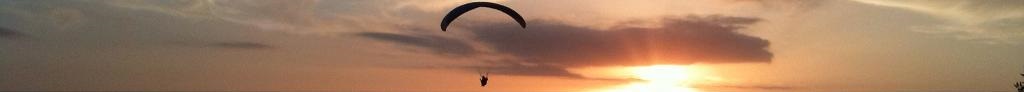 A paraglider silhouetted against a sunset sky